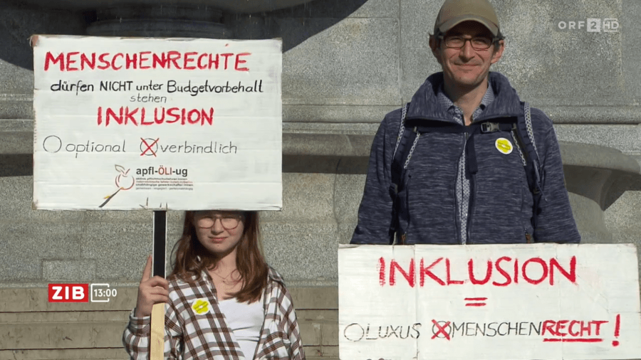 Standbild des ORF ZIB-Beitrags zur Kundgebung. Ein Mädchen und ein Mann halten jeweils ein Schild "Menschenrechte dürfen nicht unter Budgetvorbehalt stehen" und "Inklusion = Menschenrecht"